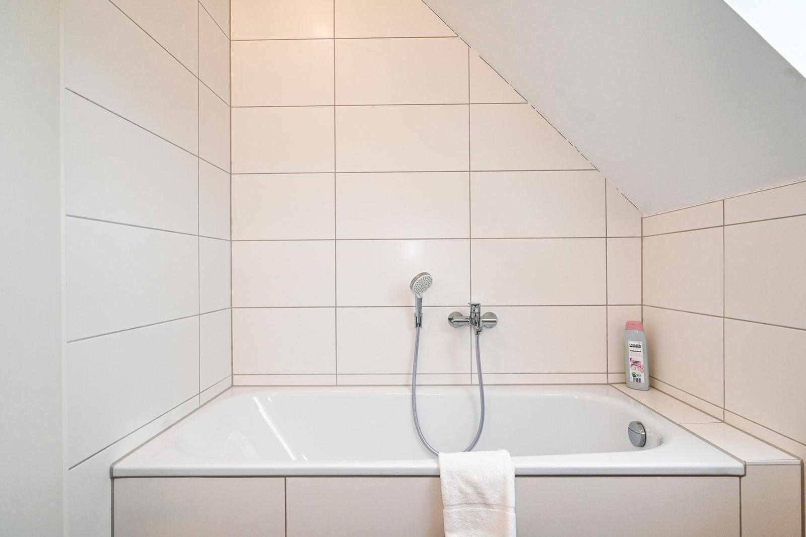 Dusche mit Handbrause und Badewanne in weißer Fliesenwand.