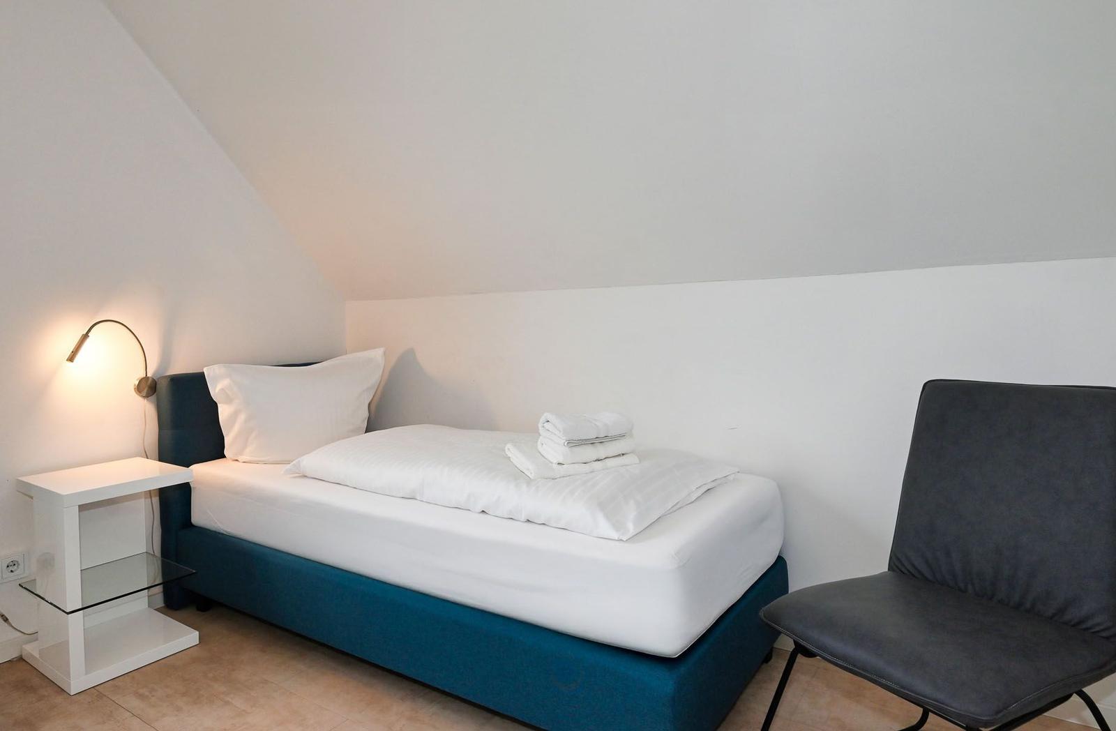 Ein Schlafzimmer mit Dachschrägen, Bett, Stuhl und Nachttisch.