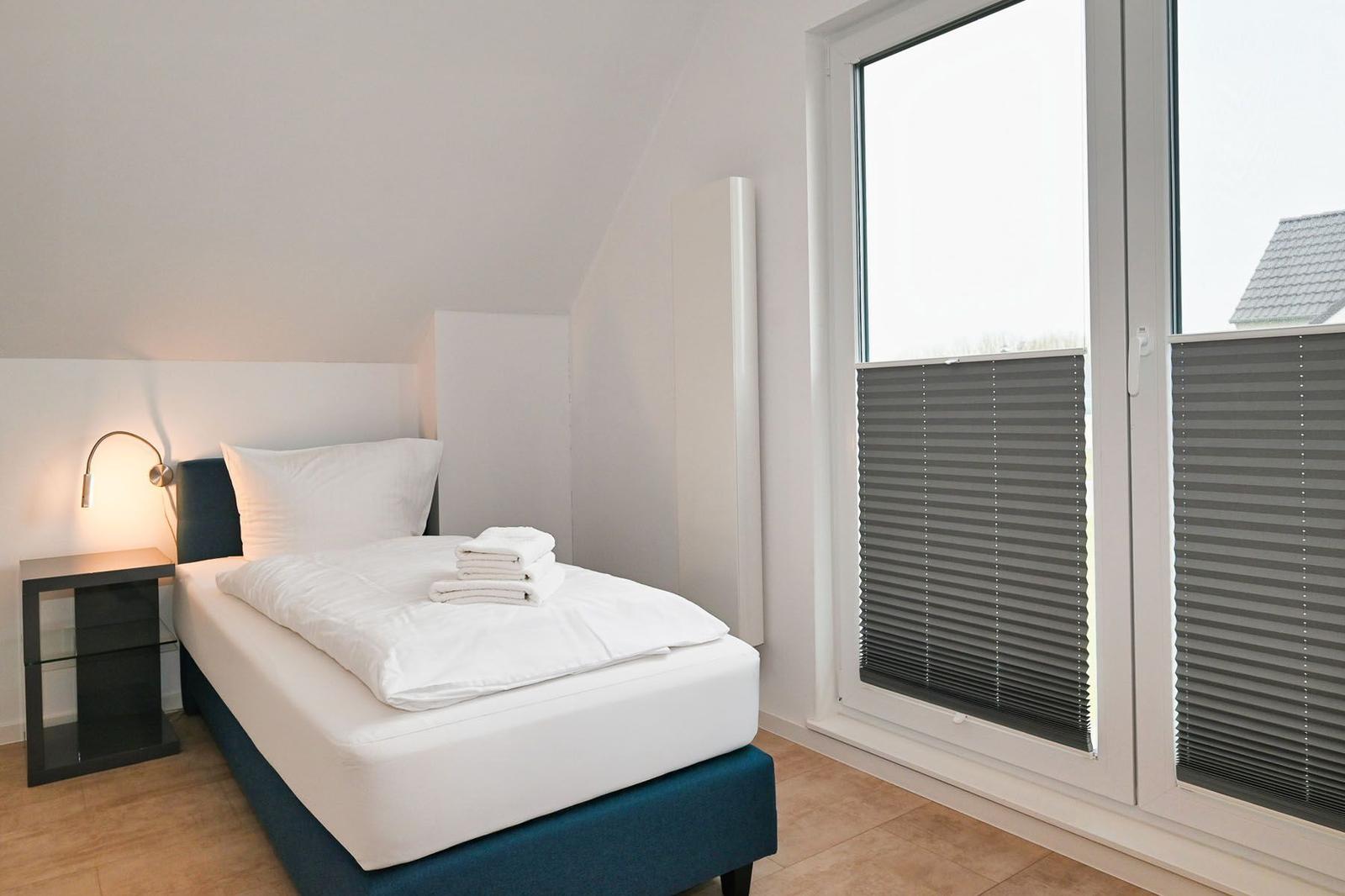 Schlafzimmer mit Bett, Nachttisch und Fenster mit Jalousie.