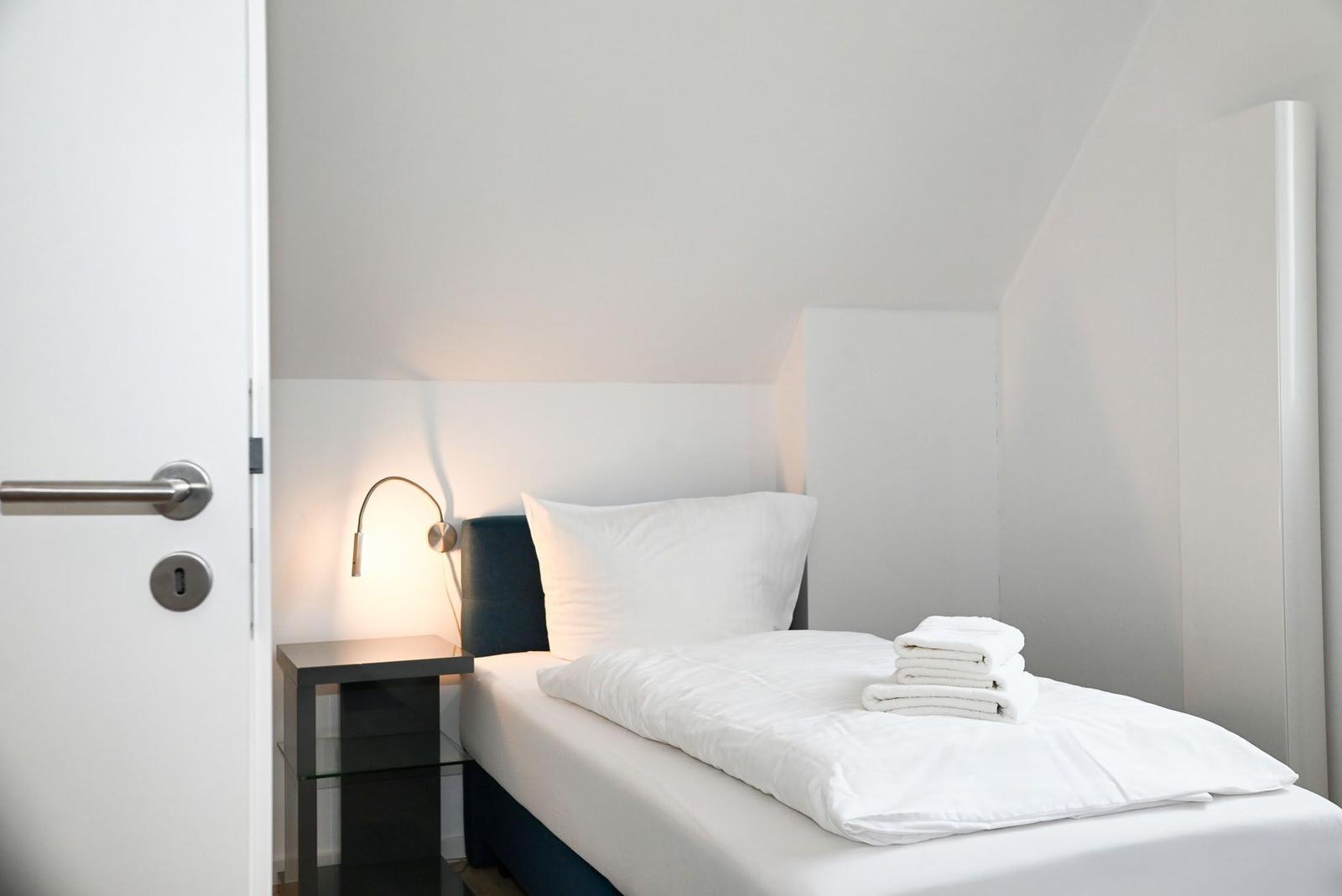 Ein Schlafzimmer mit einem Bett, einer Nachttischlampe und gefalteten Handtüchern.