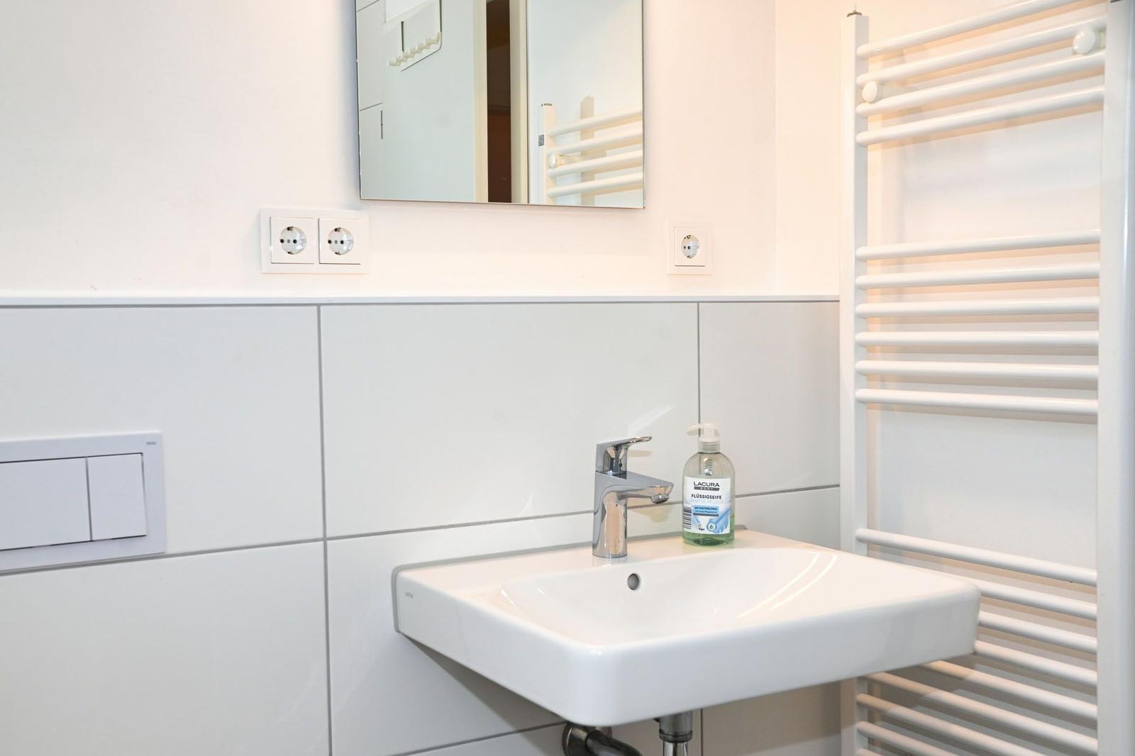 Waschbecken mit Spiegel und Handtuchhalter in weißer Wand