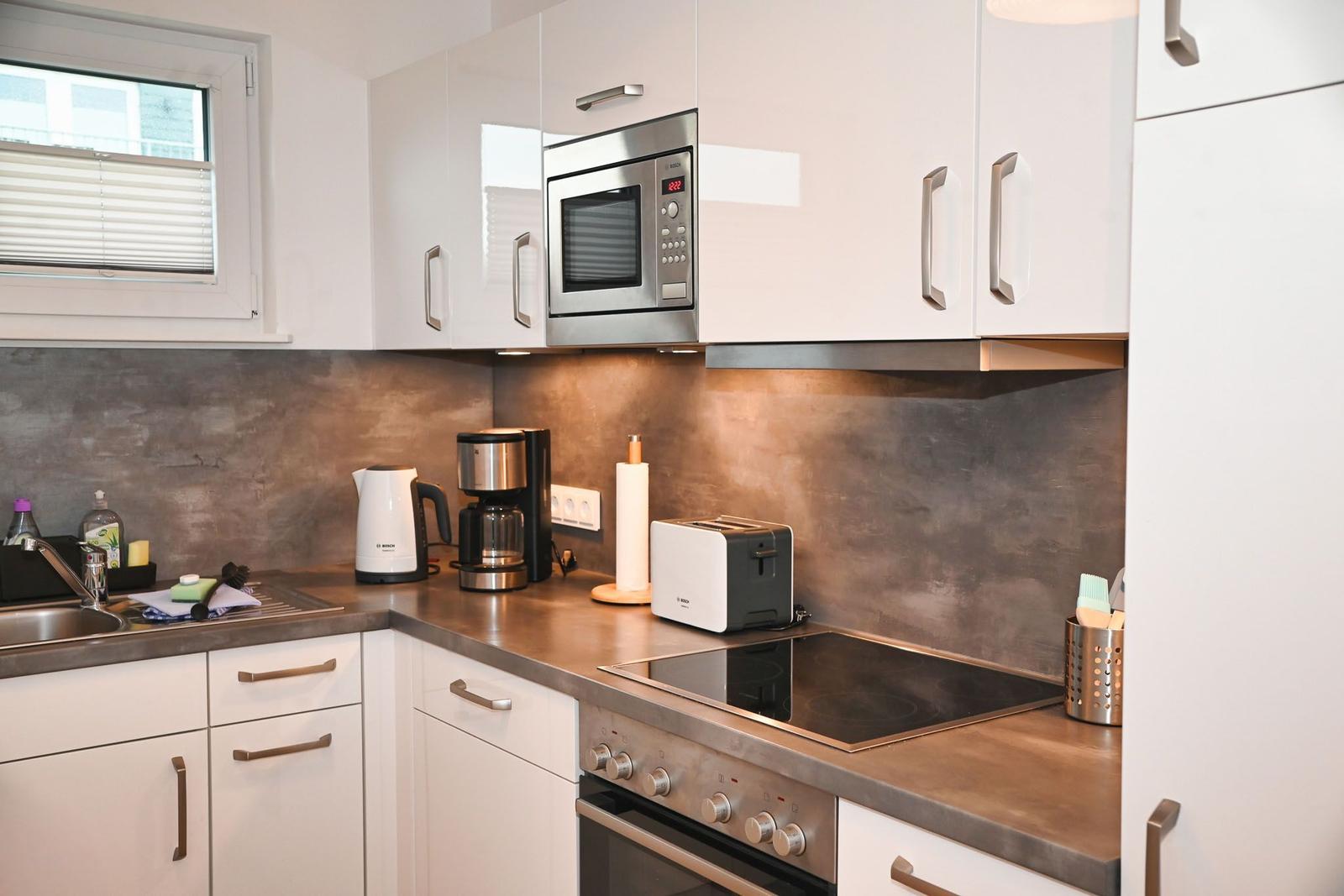 Küche mit weißen Schränken, Edelstahlgeräten und dunkler Arbeitsplatte.