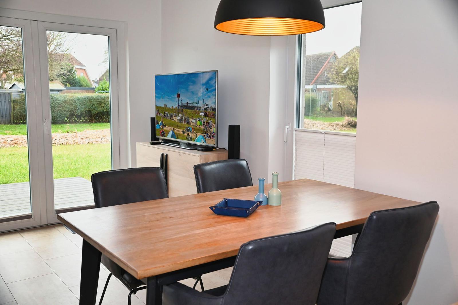 Esstisch mit Stühlen, Fernseher und Fenster zur Terrasse.
