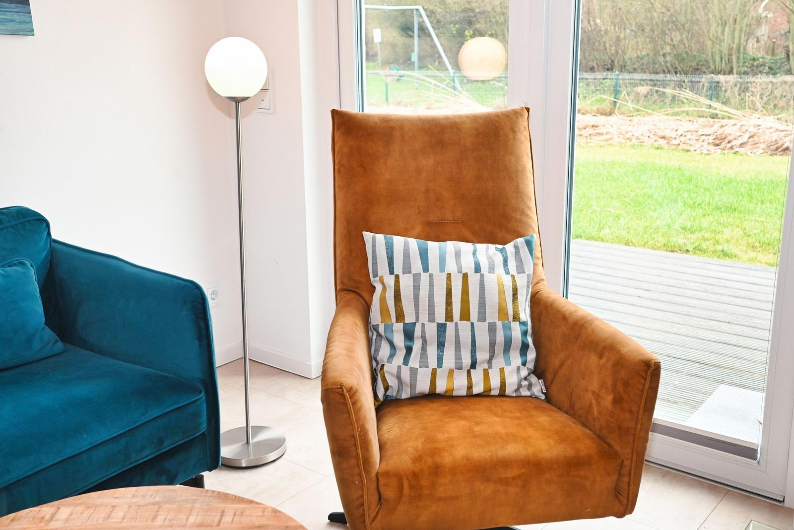 Ein braunes Sessel mit Kissen steht vor einem Fenster mit Blick auf einen Garten.