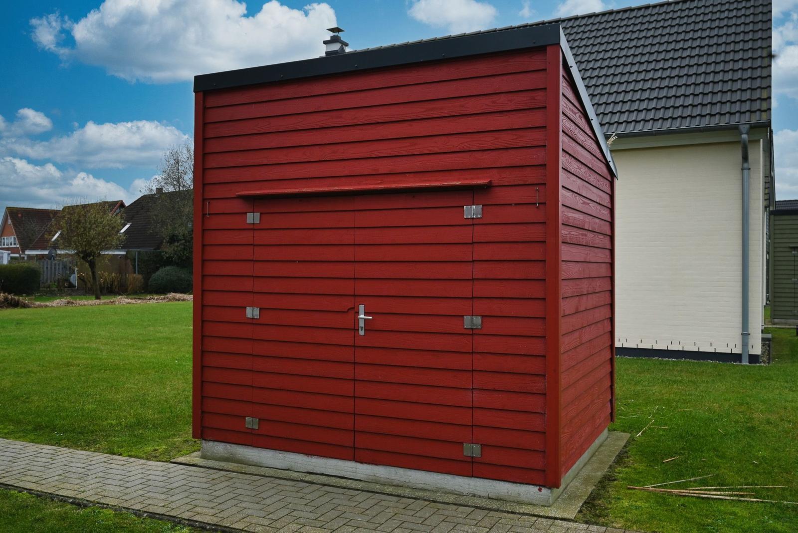 Roter Holzschuppen mit Tür und Dachrohr im Garten