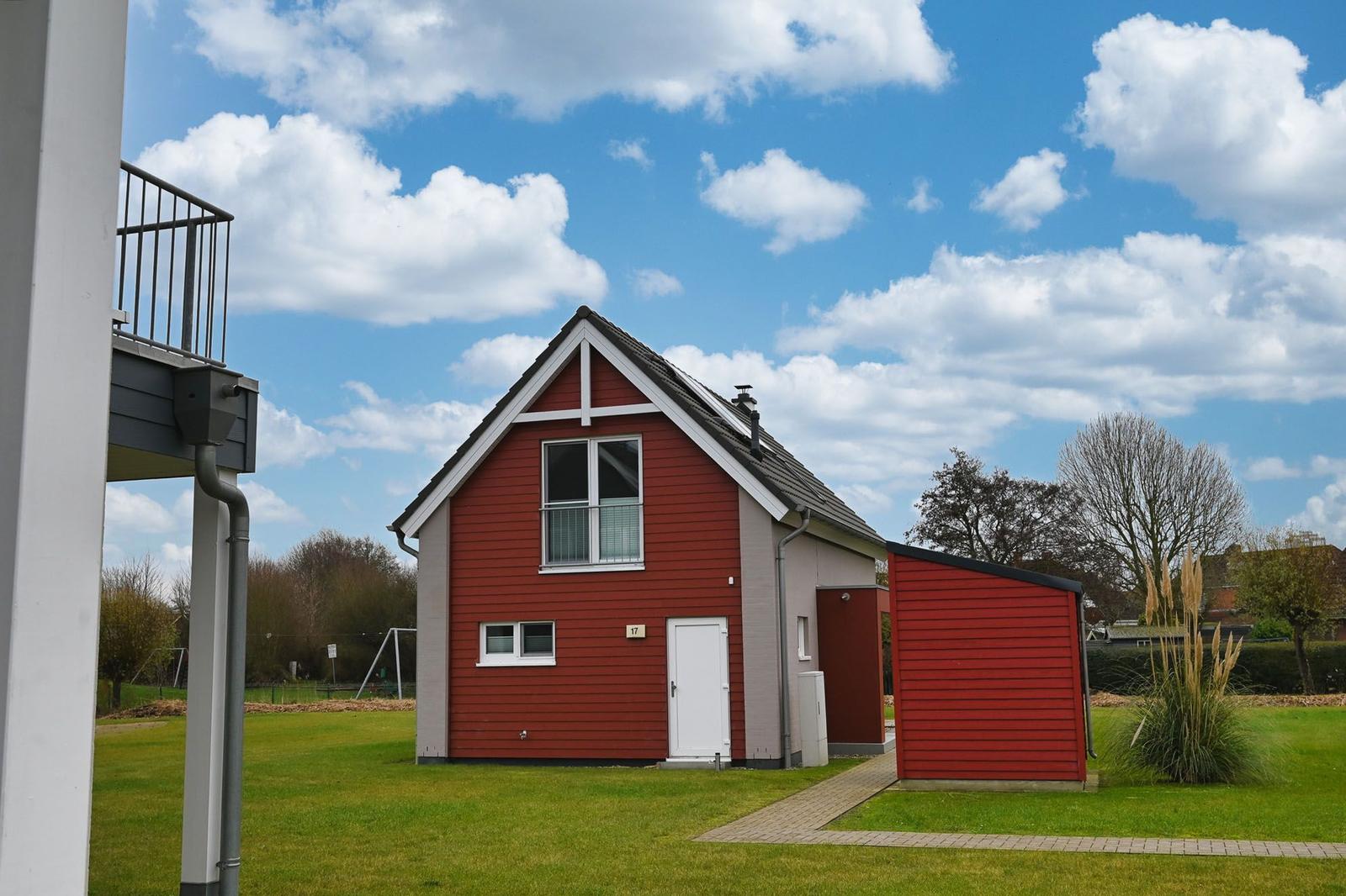 Rotes Haus mit weißer Tür und Terrasse auf grünem Grund.