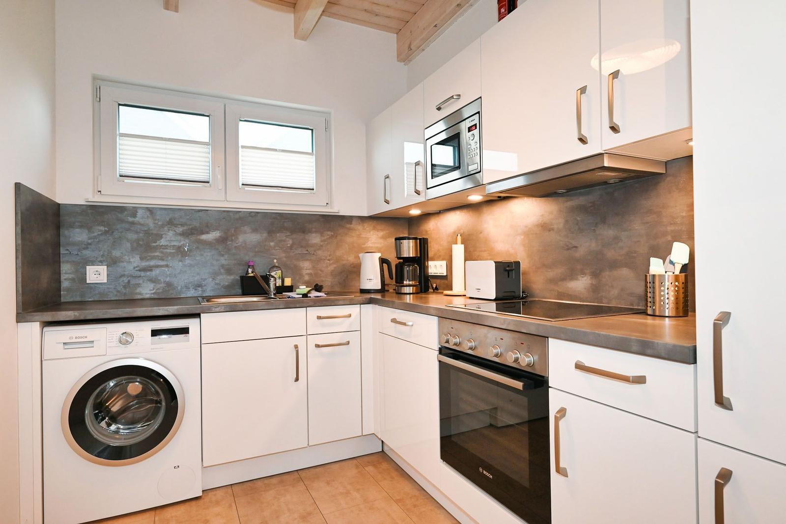 Küche mit Waschmaschine, Herd, Mikrowelle und Fenster.