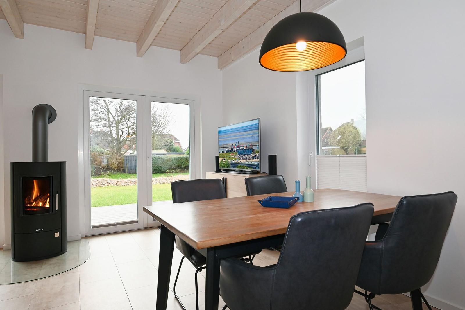 Esszimmer mit Esstisch, Stühlen, TV und Kaminofen. Durchgangstür zum Garten.