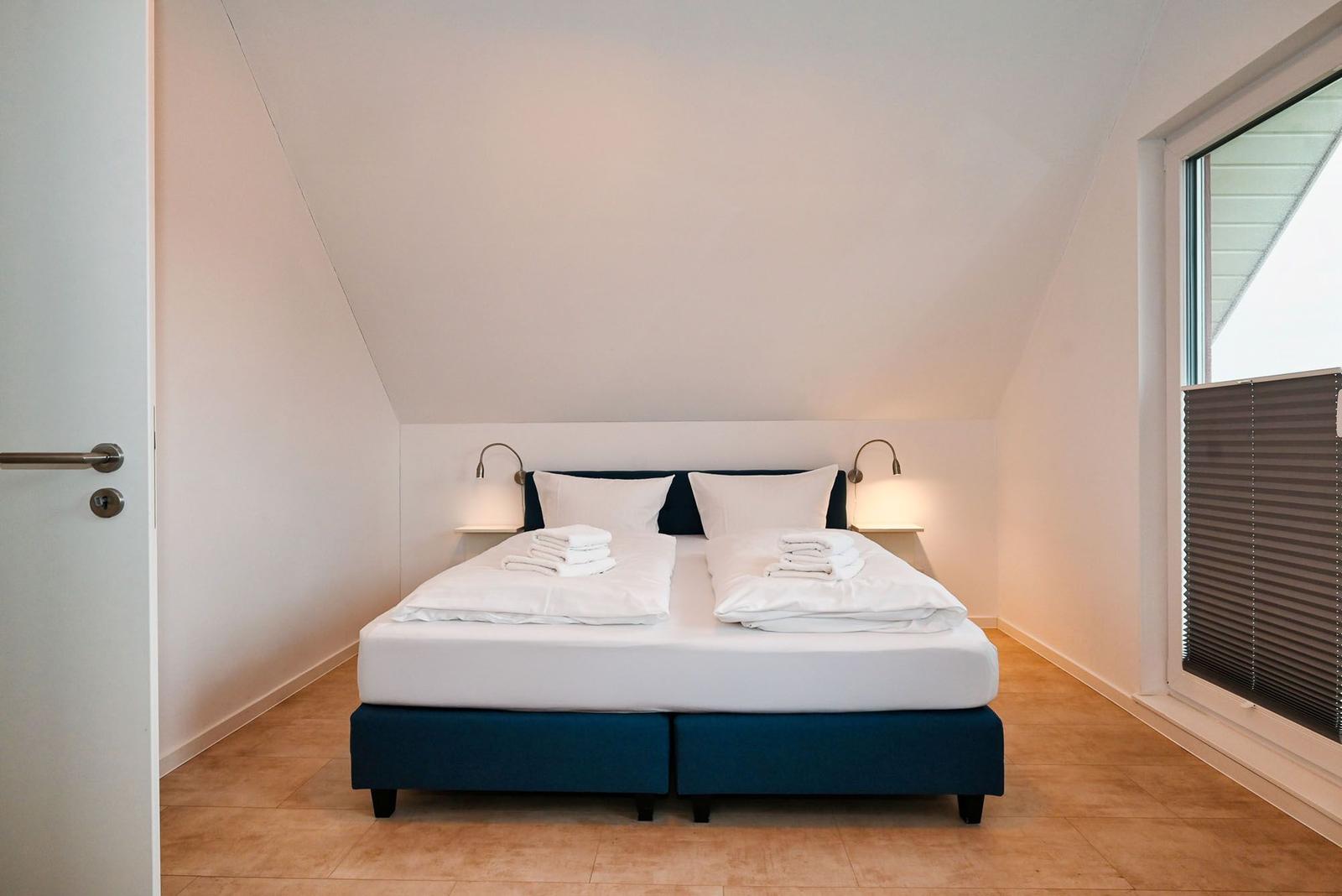 Schlafzimmer mit Doppelbett, Fenster und Wandlampen.