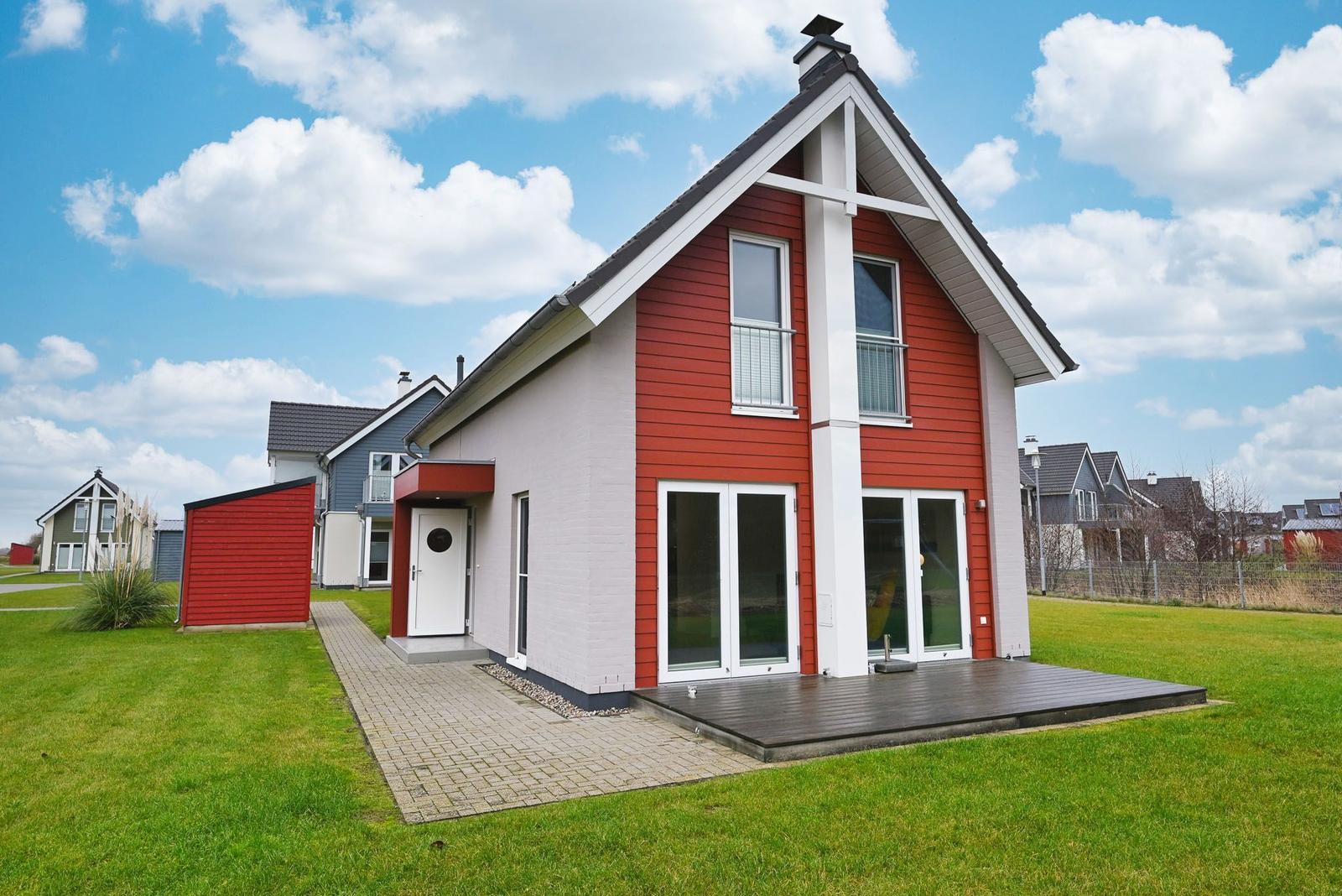 Moderne Villa mit roten und weißen Außenwänden, großem Holzdeck und grünem Rasen.