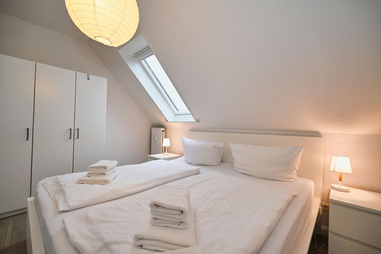 Schlafzimmer mit Dachschrägen, Bett, Nachttisch, Kleiderschrank und Dachfenster.