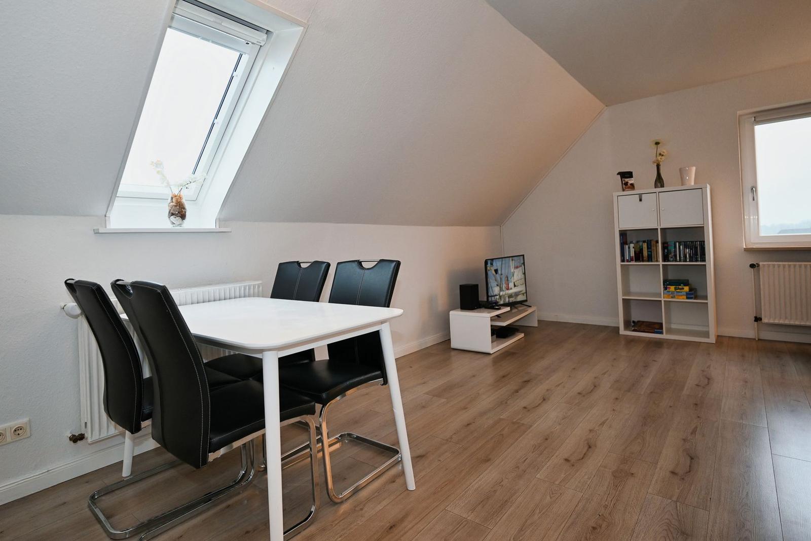 Dining area with white table, black chairs, TV, bookcase, and skylight.
