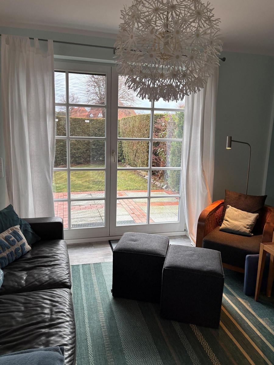 Wohnzimmer mit Sofa, Sessel und Blick auf Garten durch Glastür