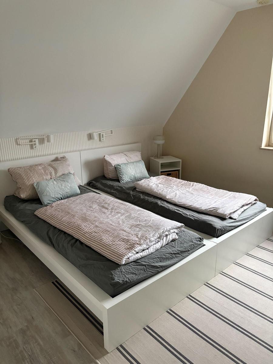 Zwei Einzelbetten mit Bettwäsche, Nachttisch und Wandlampen in einem Dachzimmer.