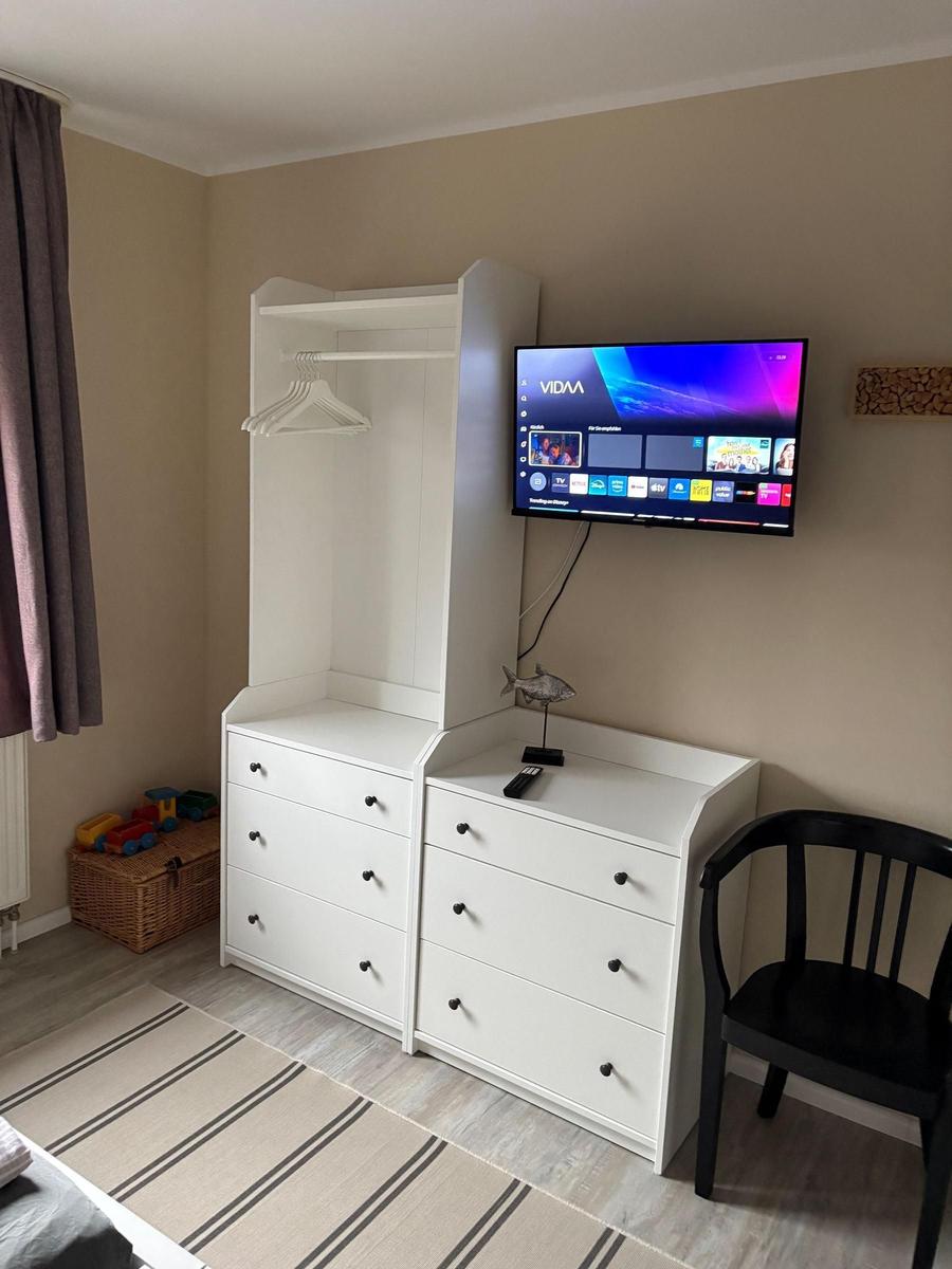 Schlafzimmer mit Kleiderschrank, Fernseher und Stuhl. Spielzeugkiste neben Fenster.