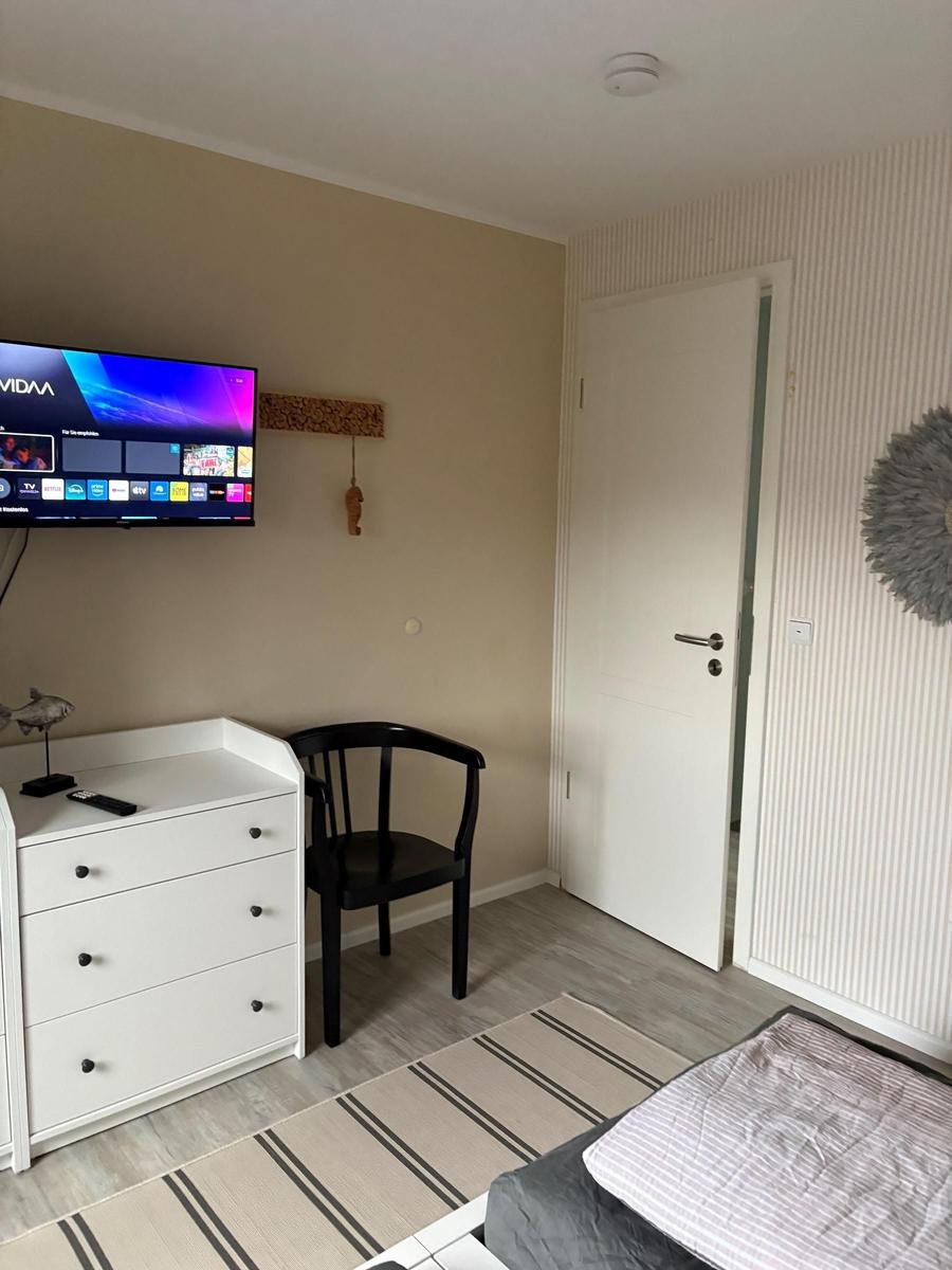 Schlafzimmer mit Bett, TV, Schrank und Stuhl. Tür und Wandverkleidung sind sichtbar.