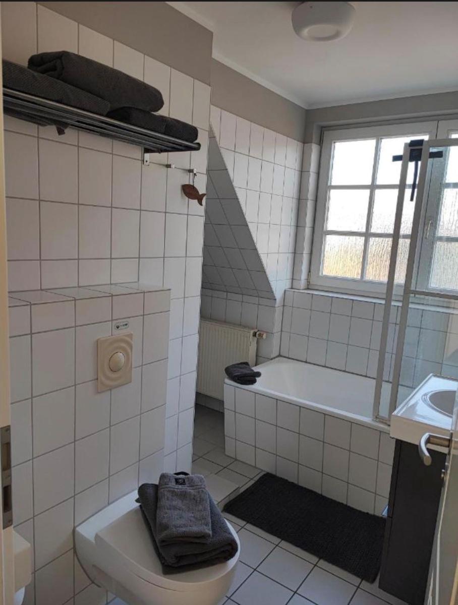 Badezimmer mit Badewanne, Toilette und Waschbecken. Weiße Fliesen und Fenster mit Blick.