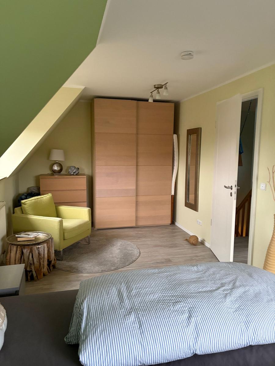 Schlafzimmer mit Bett, Schrank und Sessel unter Dachschrägen.