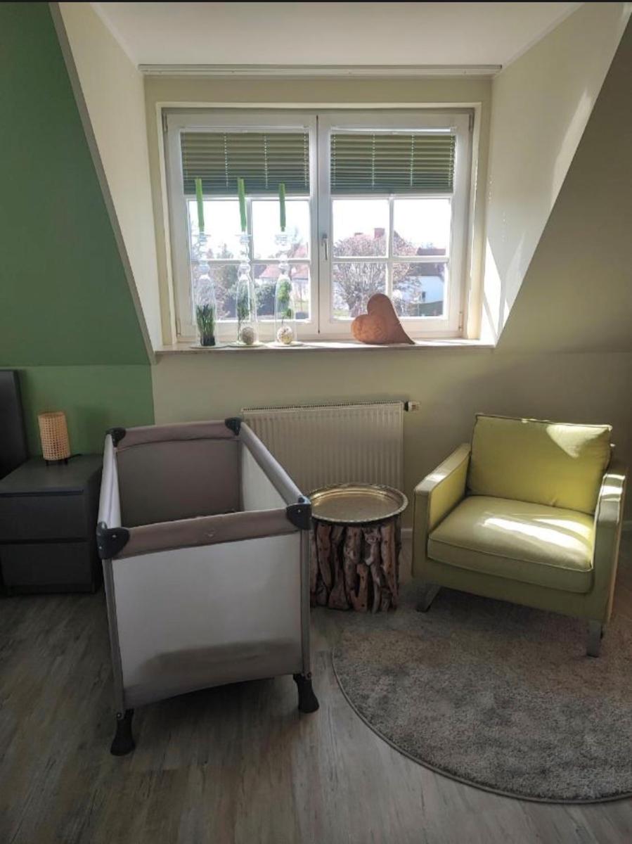 Ein Raum mit Babybett, Sessel und Fenster mit Jalousien.