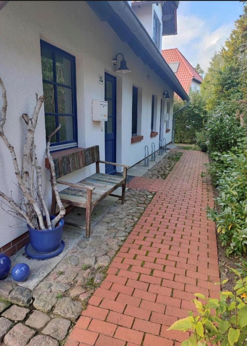 Haus mit blauer Tür, Stein- und Ziegelweg, Bank und Pflanzen im Vorgarten.