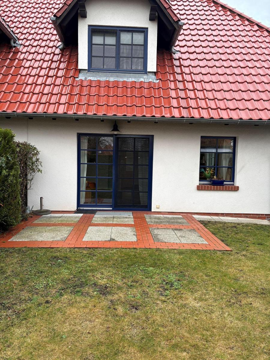 Haus mit rotem Dach, blauen Fenstern und gepflastertem Vorgarten.