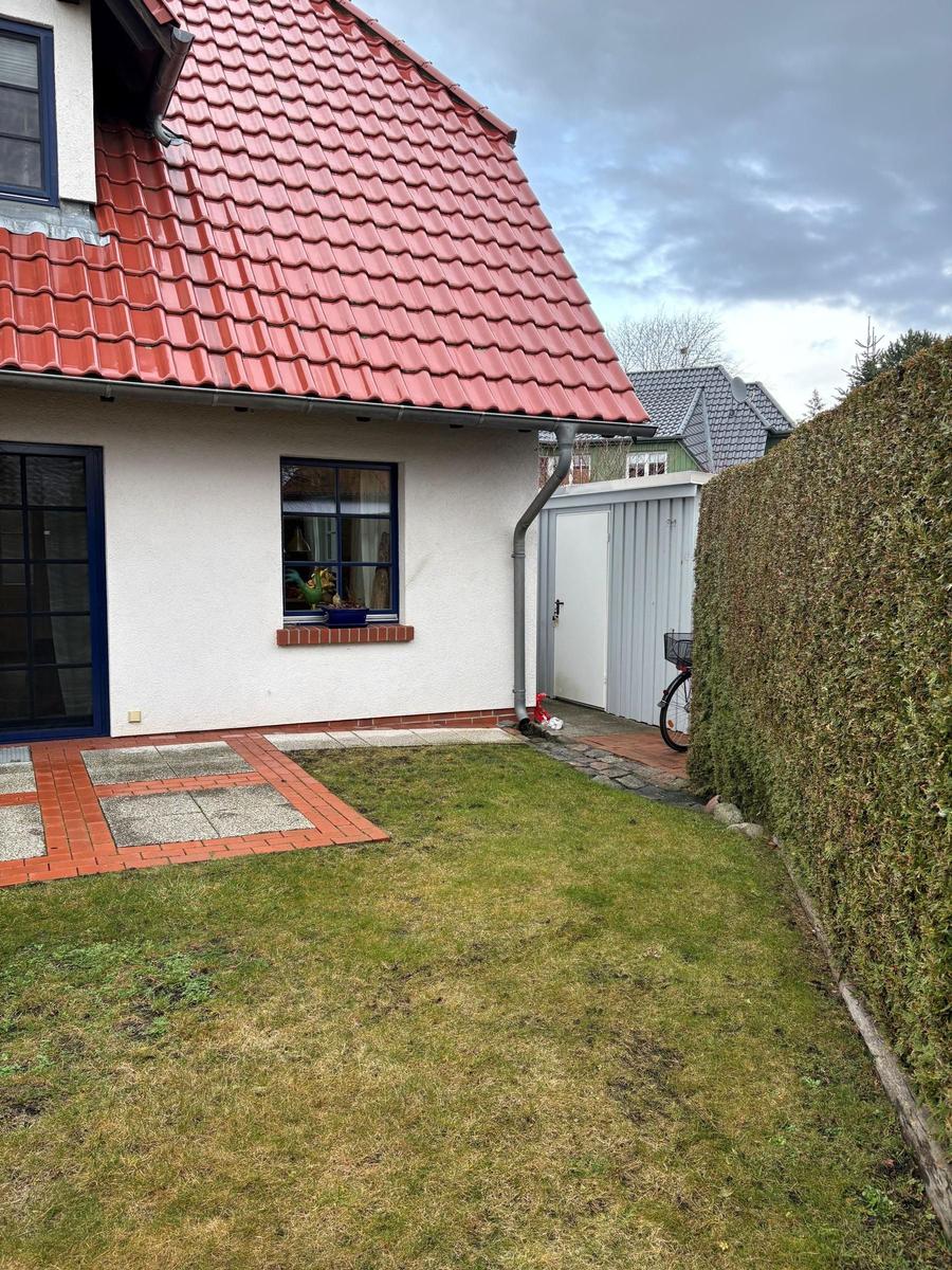 Haus mit rotem Dach, weißer Fassade und Gartenbereich mit Rasenfläche.
