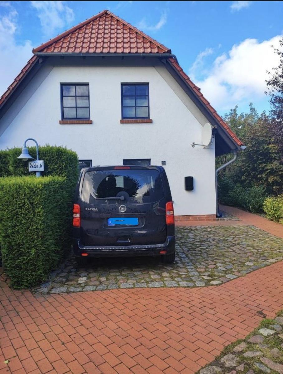 Ein Haus mit rotem Dach und weißer Fassade. Ein schwarzes Auto steht auf einem Kiesplatz.