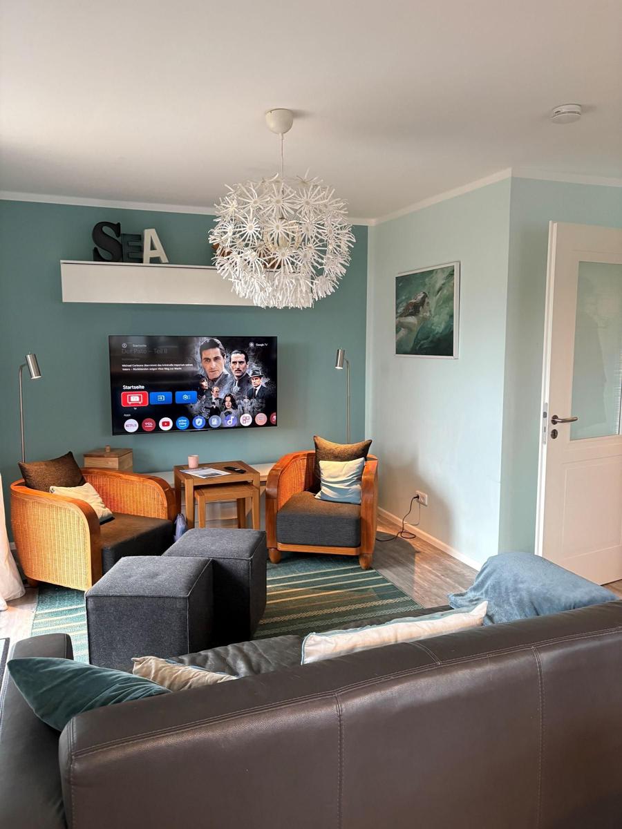 Wohnzimmer mit Sofa, Sesseln, Fernseher und Deckenleuchte.