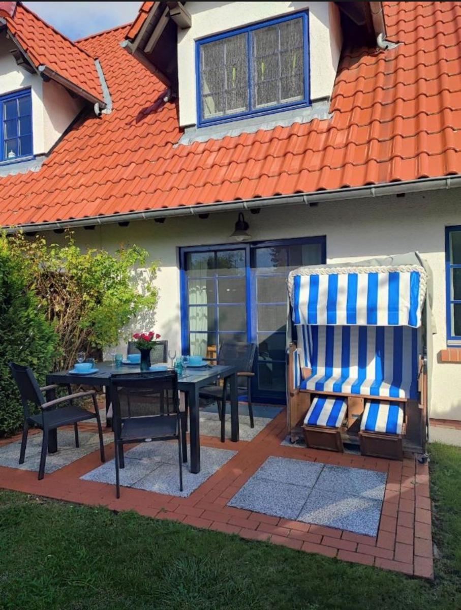 Terrasse mit Tisch, Stühlen und Strandkorb. Haus mit rotem Dach und blauen Fenstern.