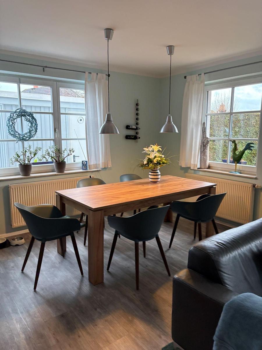 Essbereich mit Holztisch, Stühlen und Fenstern mit Blick nach draußen.