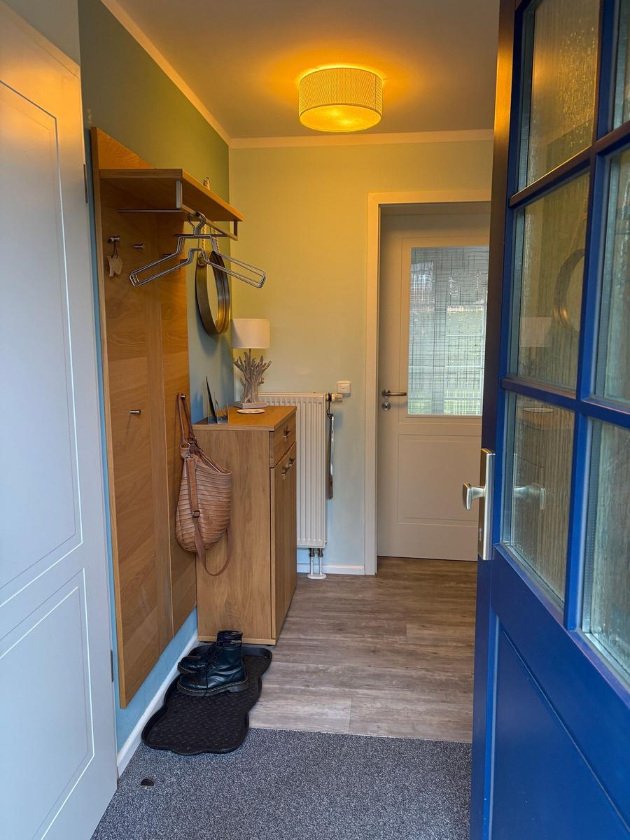 Eingangsbereich mit Holzmöbeln, Schuhen und einer Lampe. Tür und Heizung sind sichtbar.