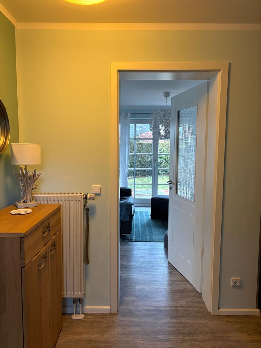 Hausgang mit Holzschrank, Heizkörper und Blick in Wohnbereich mit Fenster.