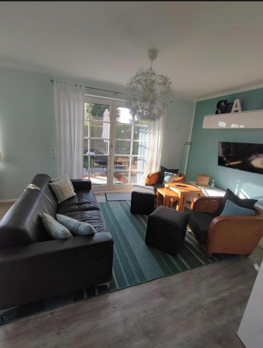 Wohnzimmer mit Sofa, Sessel und TV. Durchgang zur Terrasse mit Glastür.
