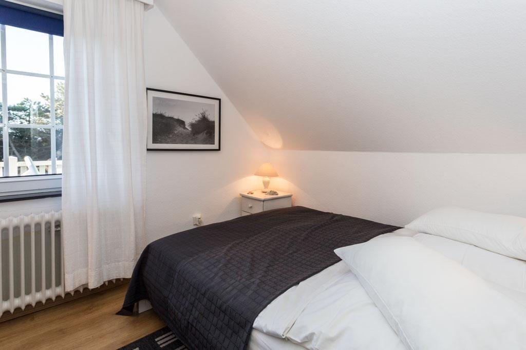 Schlafzimmer mit Dachschrägen, Bett, Nachttisch und Fenster mit Vorhängen.