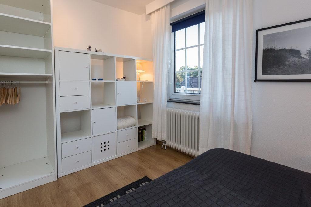 Schlafzimmer mit Bett, Kleiderschrank und Fenster mit Vorhängen.