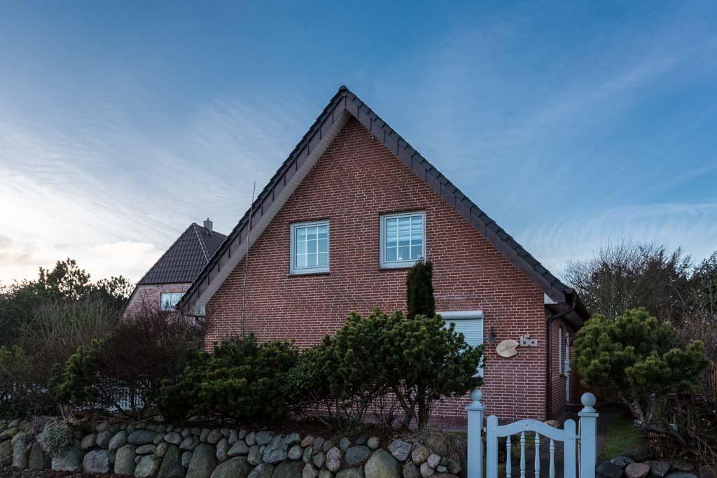 Rotes Backsteinhaus mit Dachgauben und kleinen Bäumen im Vorgarten.