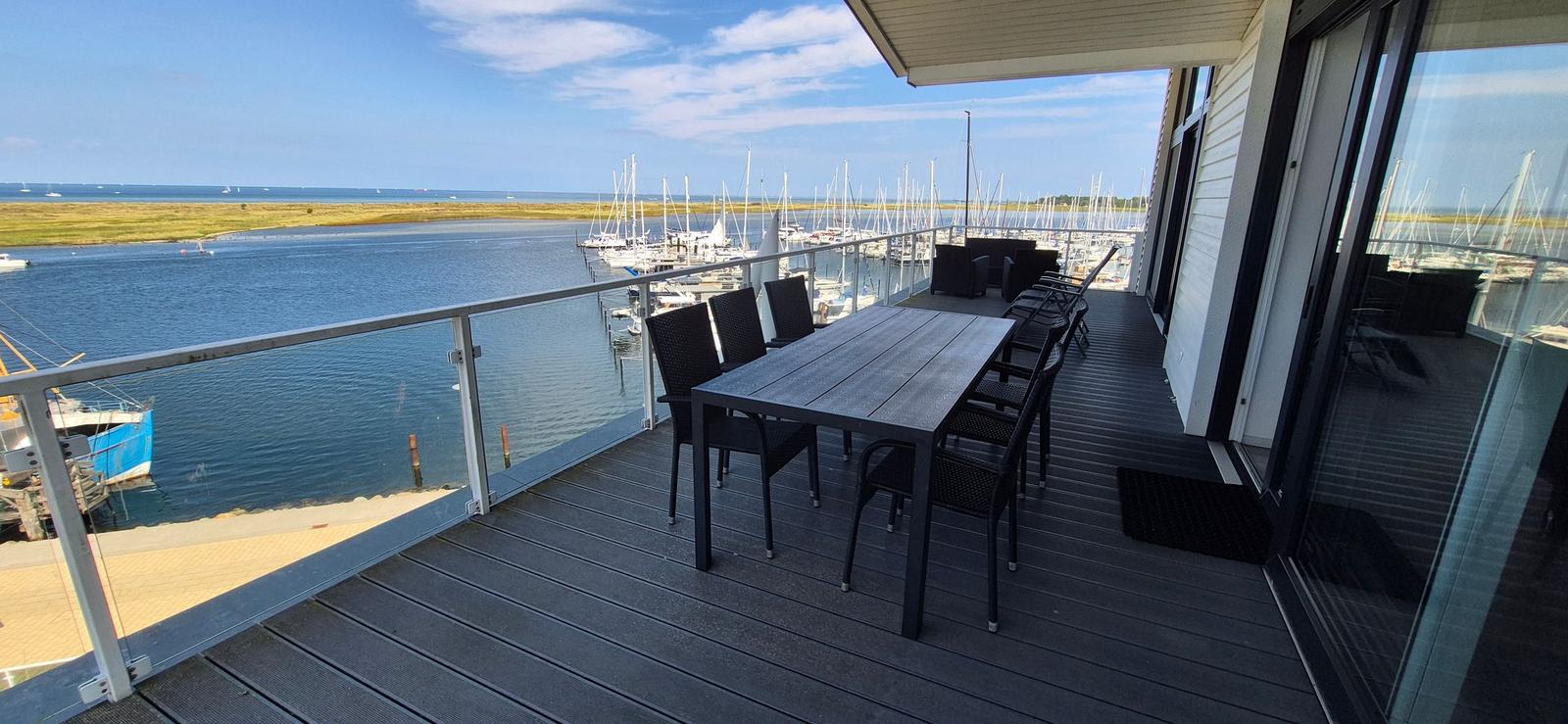 Terrasse mit Tisch und Stühlen, Blick auf Hafen mit Segelyachten.