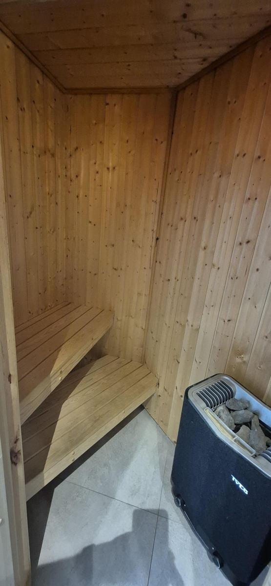 Sauna mit Holzwand und Sitzbank, daneben Heizgerät mit Steinen.