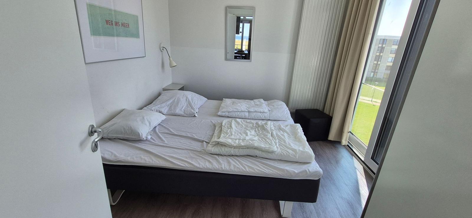 Schlafzimmer mit Doppelbett, Spiegel und Fensterblick auf Grünfläche.