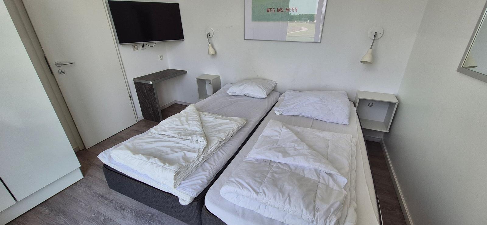Zwei Einzelbetten, Fernseher, Schreibtisch und Wandlampen im Schlafzimmer.