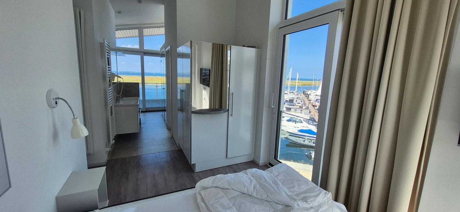 Schlafzimmer mit Blick auf Hafen und Meer. Neben dem Bett befindet sich ein Flur mit Bad.