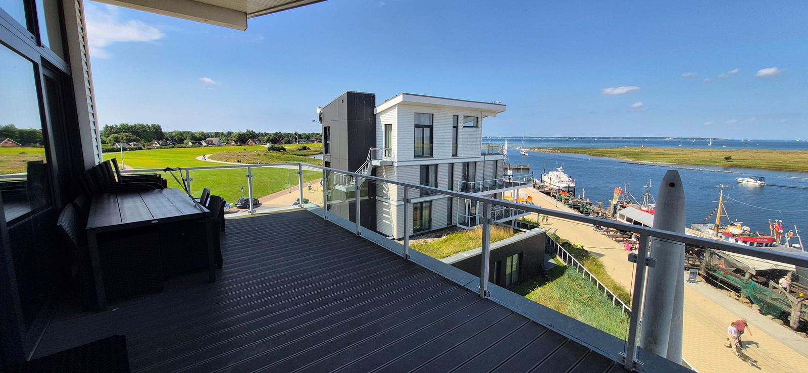 Terrasse mit Blick auf Wasser, Bootshäfen und grüne Landschaft.