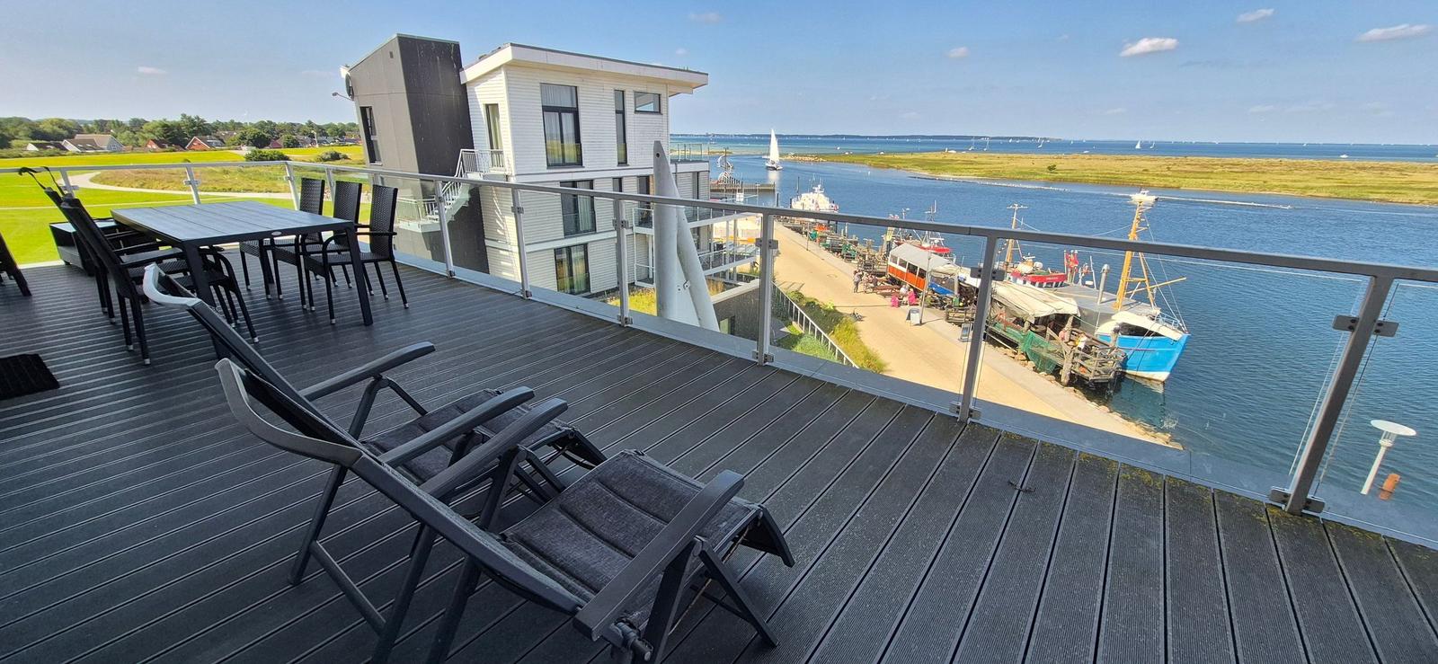 Terrasse mit Sitzgelegenheiten und Blick auf Hafen und Wasser.