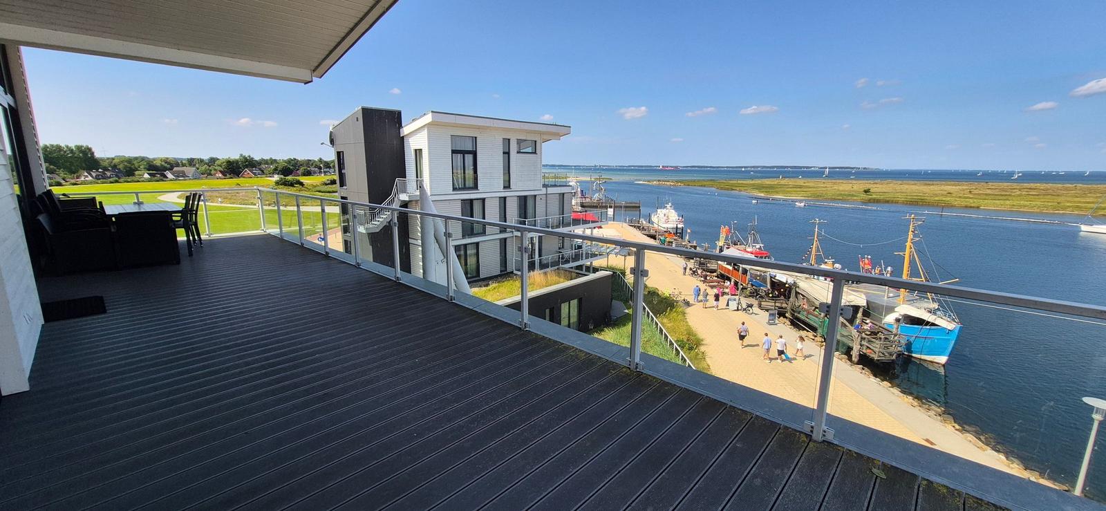 Terrasse mit Blick auf Hafen und Wasser. Moderne Gebäude und Boote sind sichtbar.