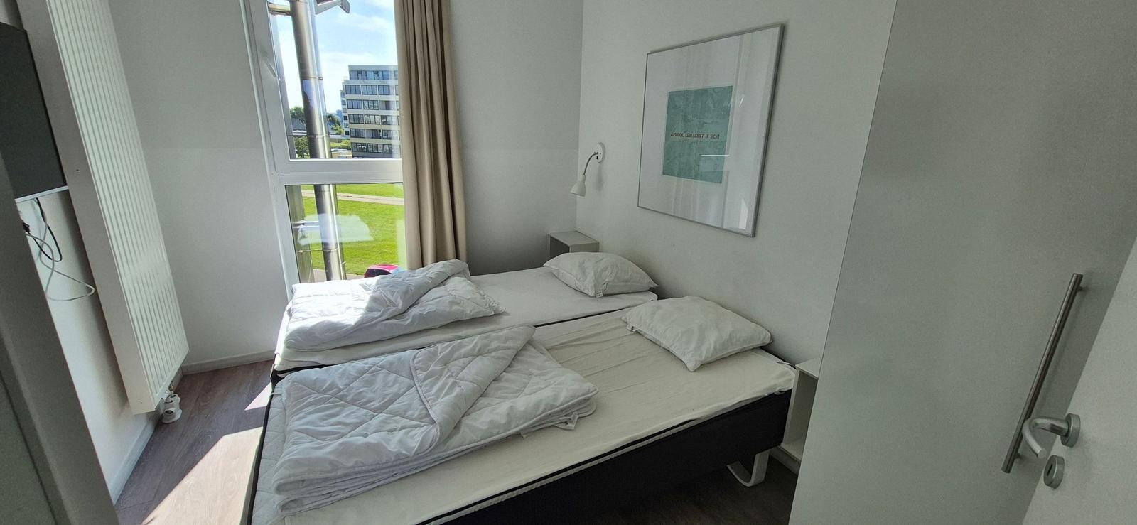 Zimmer mit zwei Einzelbetten, Fenster mit Blick auf Grünfläche und Gebäude.