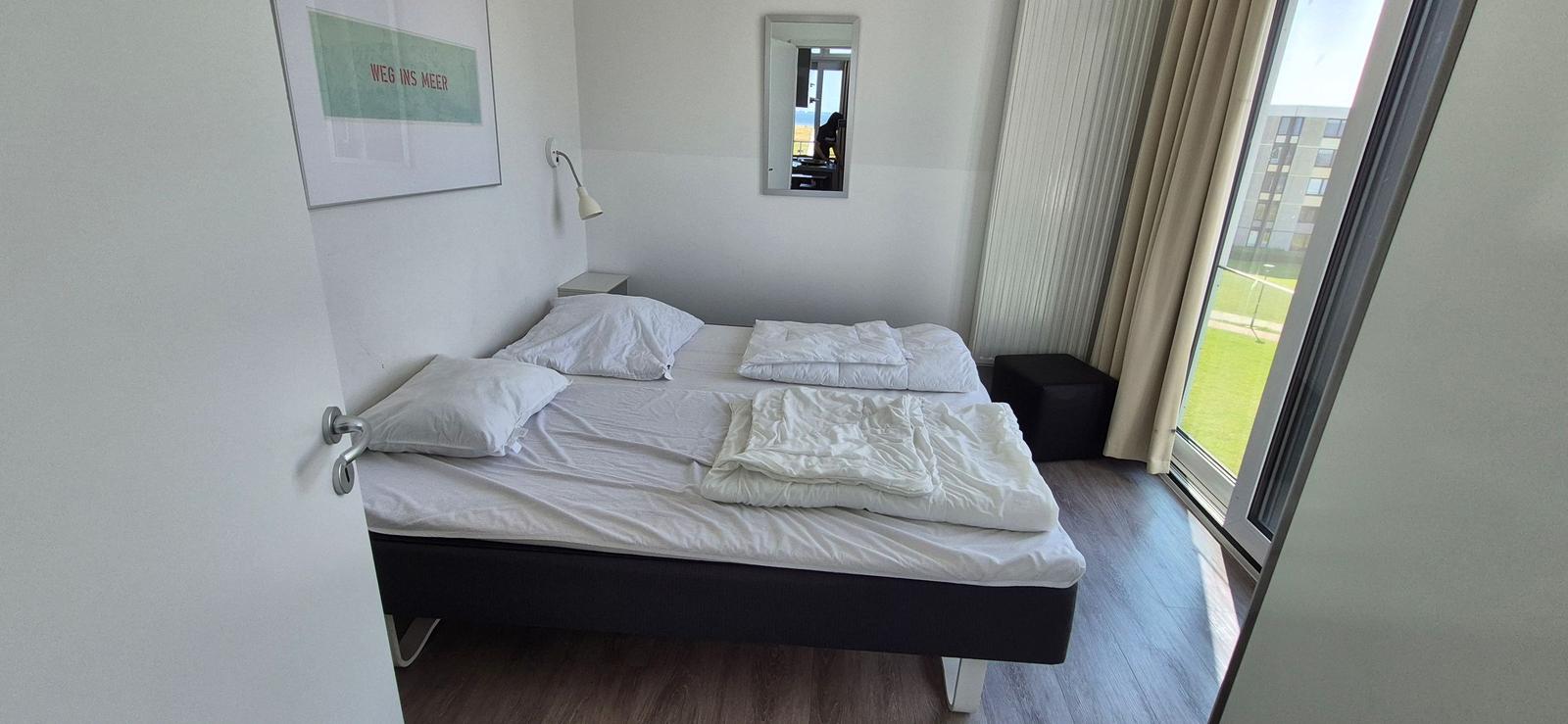 Schlafzimmer mit Bett, Spiegel und Fenster zur Aussicht.