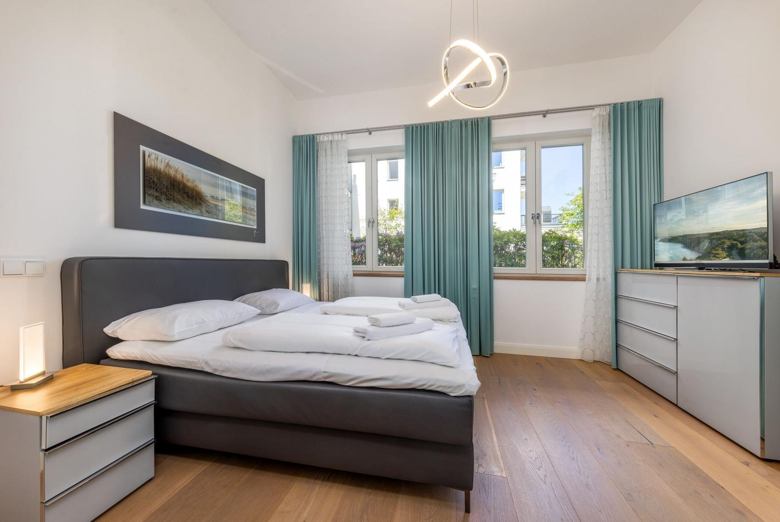 Schlafzimmer mit Bett, TV und Fenster mit Blick auf Balkon.