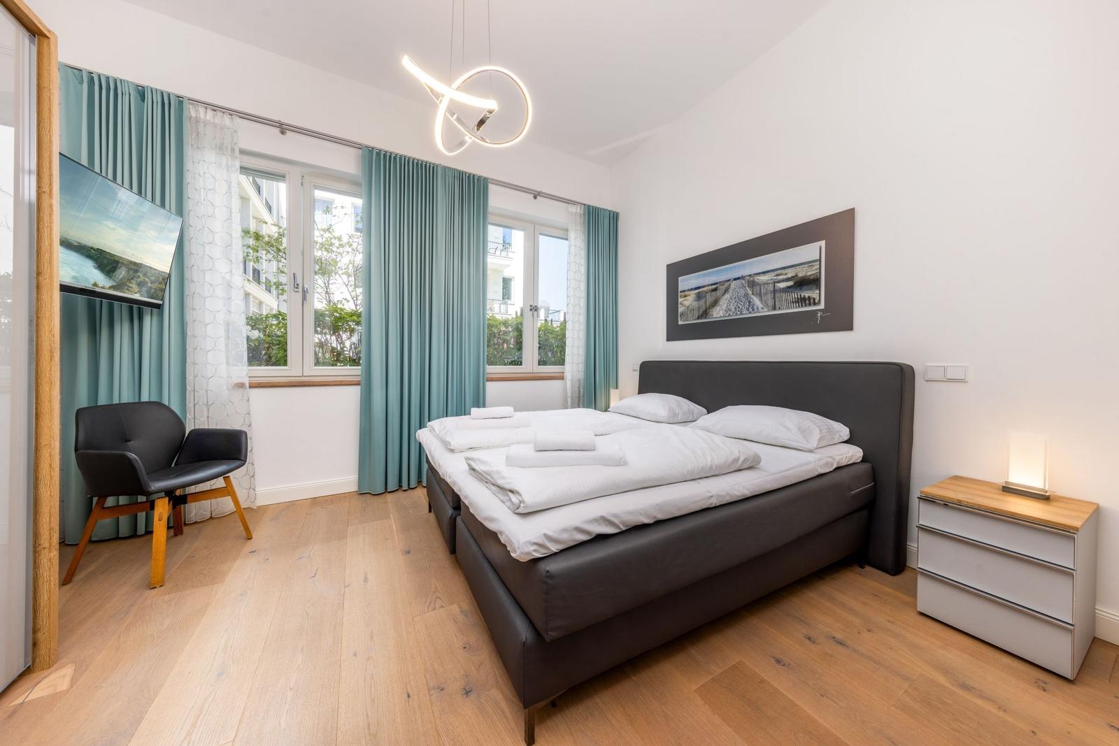 Schlafzimmer mit Bett, Nachttisch und Fenster mit Vorhängen.