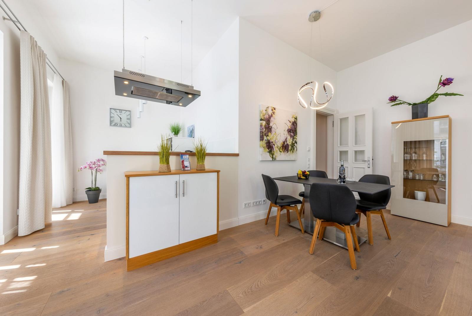 Essbereich mit Tisch, Stühlen und Glasvitrine. Küchenbereich mit Dunstabzug.