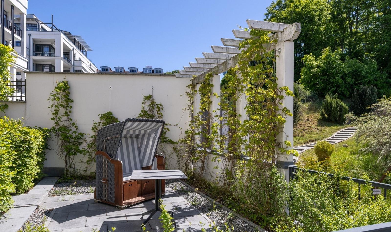 Terrasse mit Liegestuhl, Tisch und Pergola. Hinterhof mit grüner Umgebung und Steinweg.